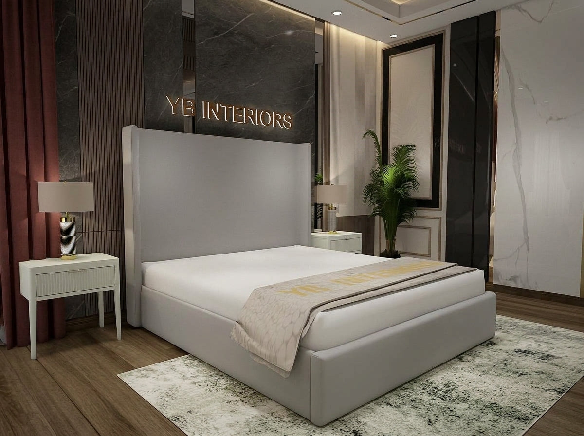 A modern upholstered bed with a tall rectangular headboard and low footboard in light gray fabric, shown in a styled bedroom. The bed is dressed in white bedding with a beige throw featuring gold lettering.