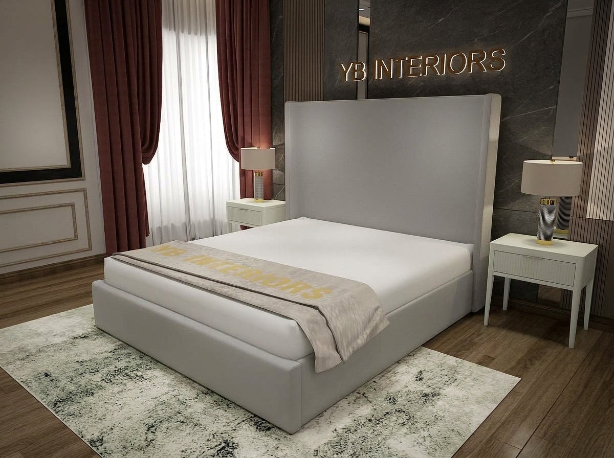 A modern upholstered bed with a tall rectangular headboard and matching base, shown in a styled bedroom. The bed is dressed in white bedding with a beige throw blanket featuring gold lettering.