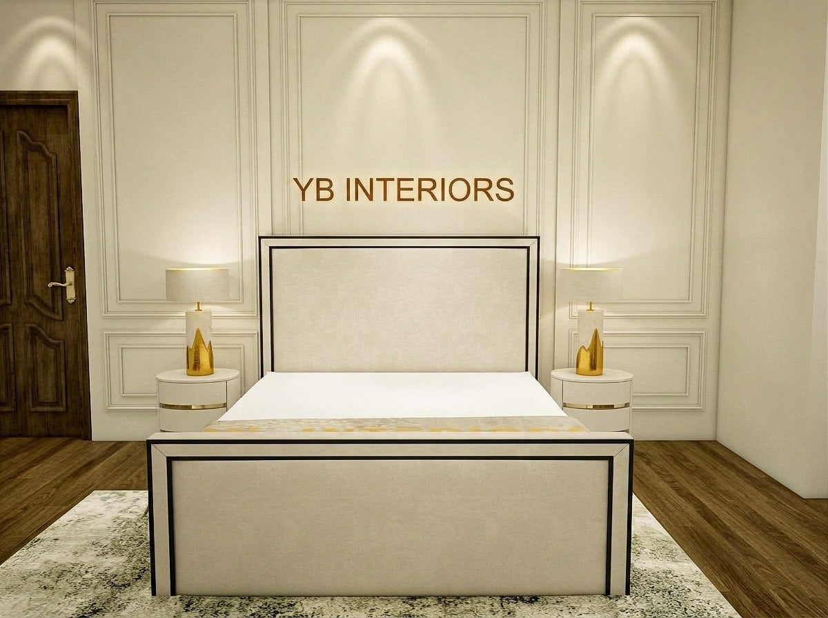 A modern upholstered bed with a light beige headboard and footboard, framed in black, shown in a styled bedroom setting. The room features white paneled walls, recessed lighting, two white nightstands with gold lamps, and a patterned rug.