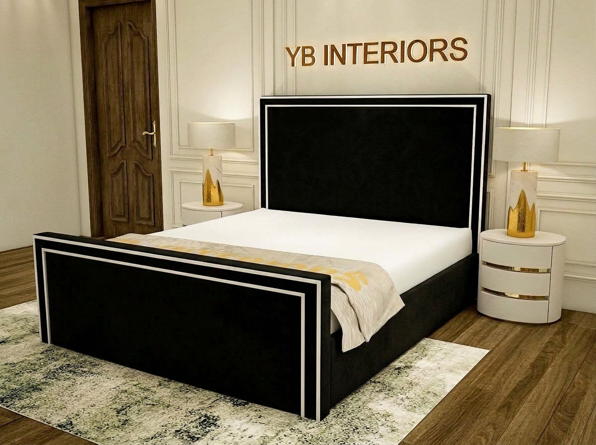 A modern black upholstered bed frame with white trim, shown in a styled bedroom setting with a white mattress, patterned rug, bedside tables, and lamps. The brand name 'YB INTERIORS' is visible on the wall above the headboard.