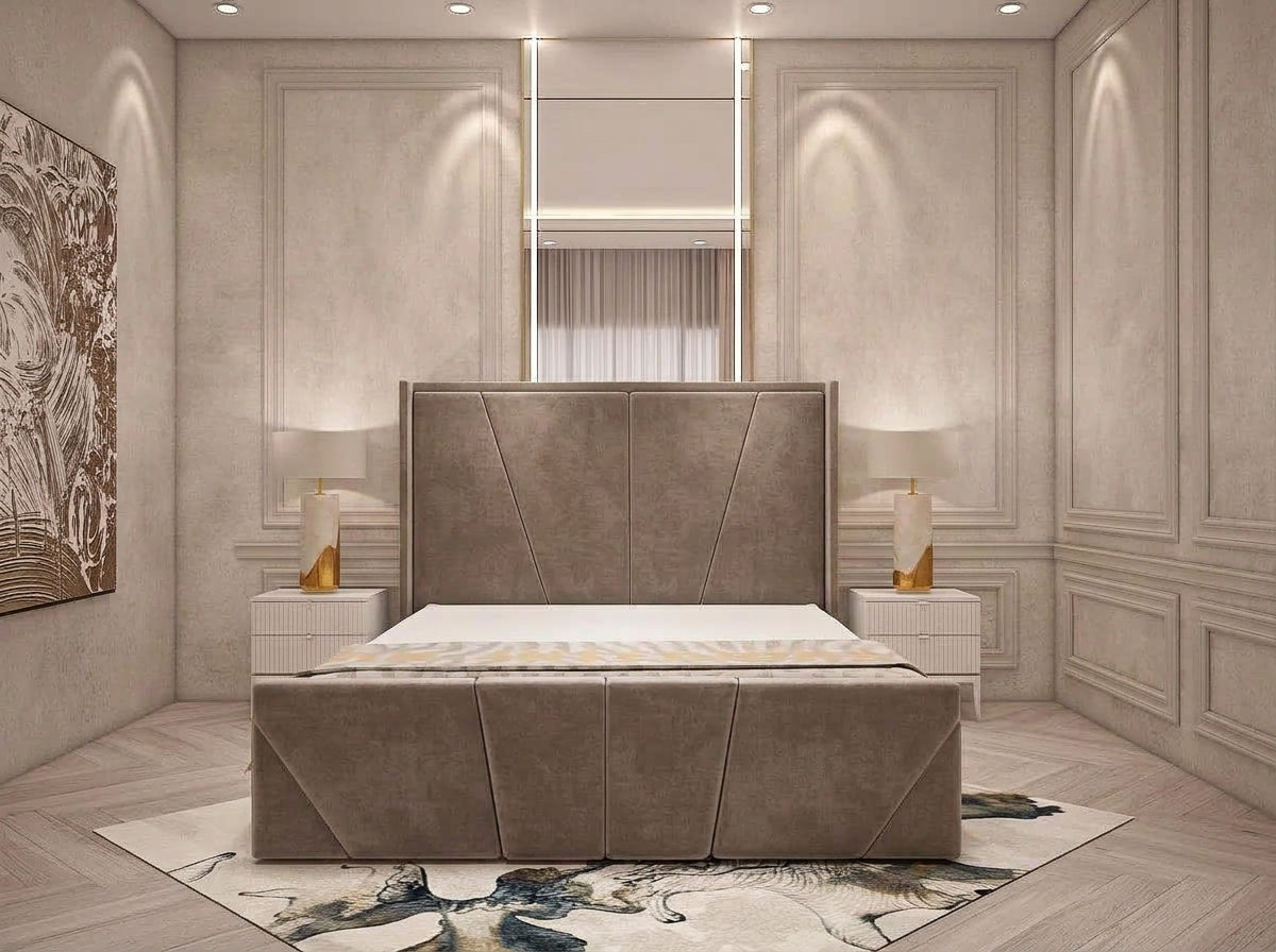 A modern upholstered bed with a tall panel headboard and matching footboard, shown in a styled bedroom with cream walls, built-in lighting, side tables, lamps, and a patterned rug.