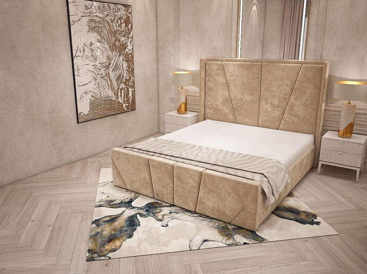 A modern upholstered bed with a tall segmented headboard and matching footboard in a warm beige fabric, shown in a styled bedroom setting with a patterned rug, bedside tables, lamps, and wall art.