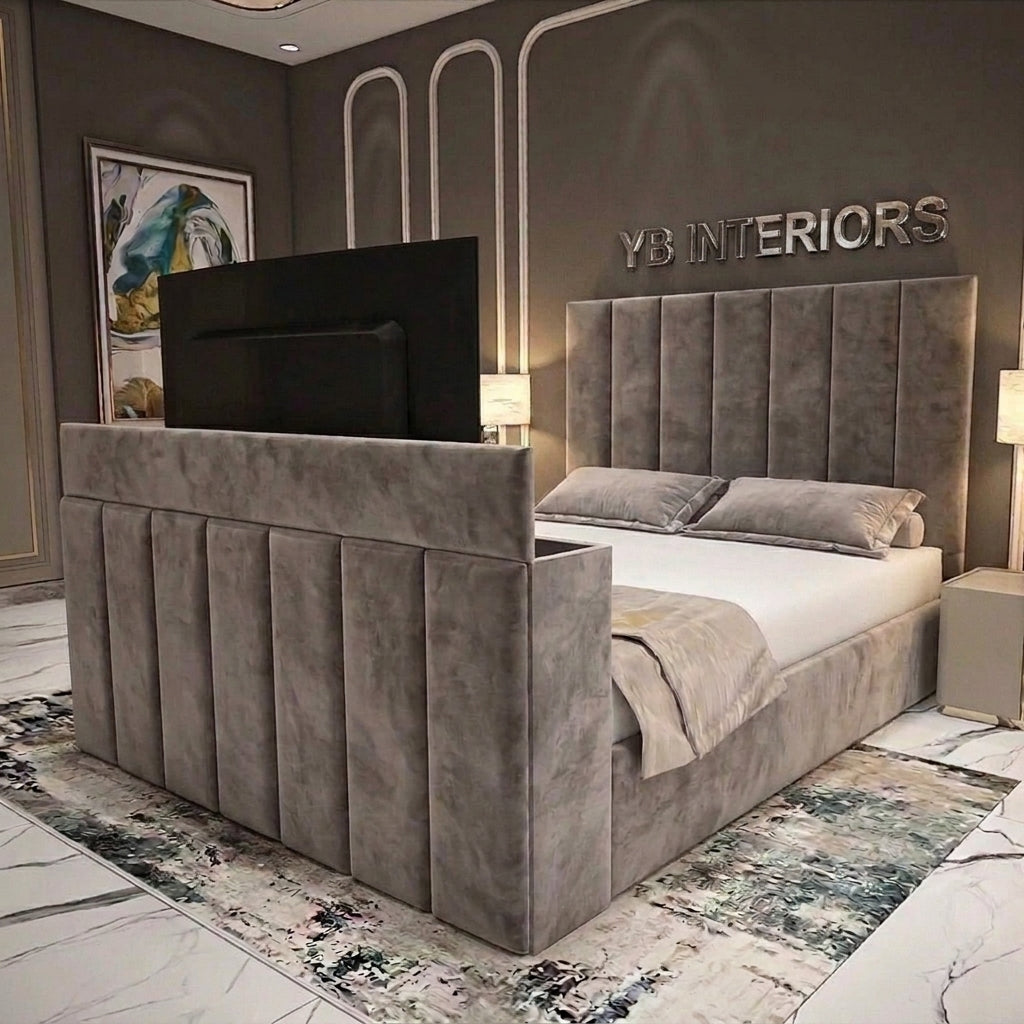 A modern upholstered bed with a tall channel-tufted headboard and matching footboard in gray velvet, shown in a styled bedroom. The bed is dressed in white bedding and a light gray throw, with a black TV mounted above the headboard.