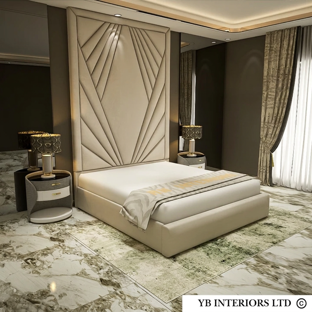 A luxurious platform bed frame with a high headboard, upholstered in a light beige fabric, flanked by two bedside tables with lamps. The bed is positioned against a wall with a geometric pattern.