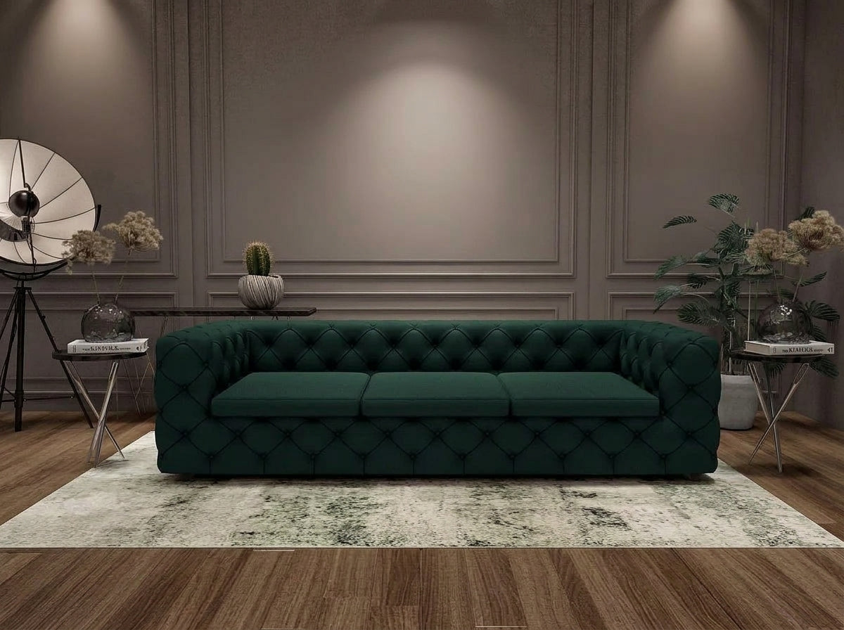 A dark green tufted velvet sofa placed in a styled living room with wood flooring, a patterned rug, side tables, plants, and wall decor.
