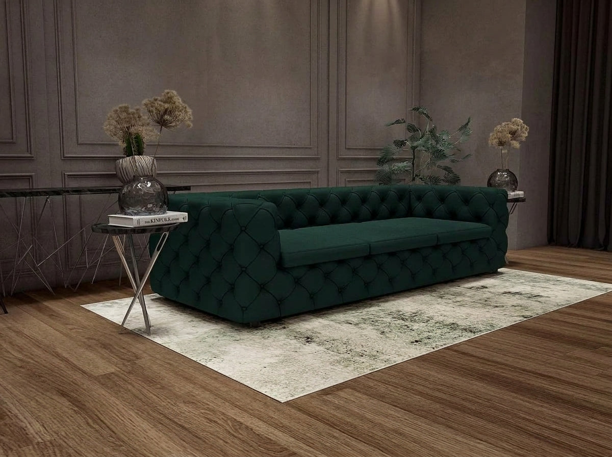 A dark green tufted velvet sofa placed on a light patterned rug in a styled living room with wood flooring, side tables, and decorative vases.