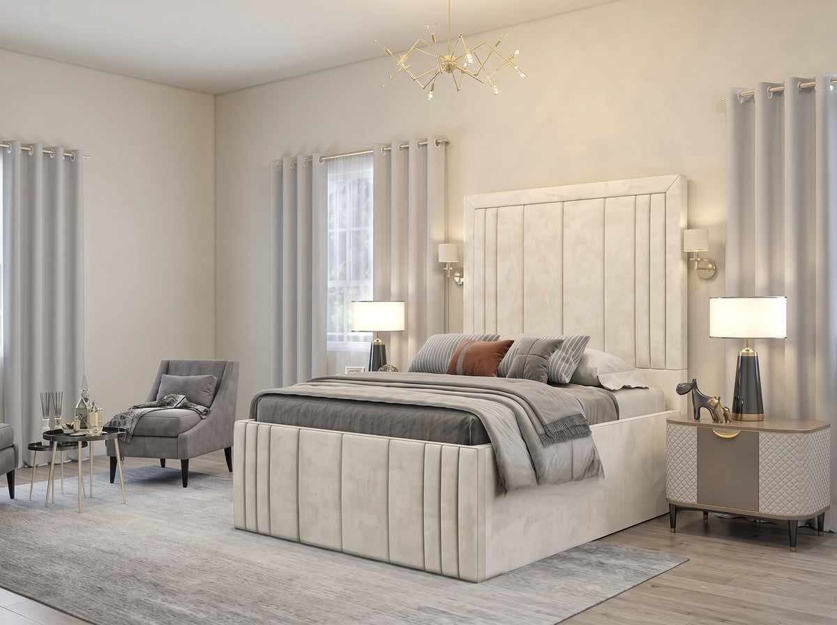 A modern bedroom featuring a large upholstered bed with a tall vertical headboard and matching footboard, styled with gray and brown bedding. The room has beige walls, light gray curtains, a gray armchair, and matching bedside tables with lamps.
