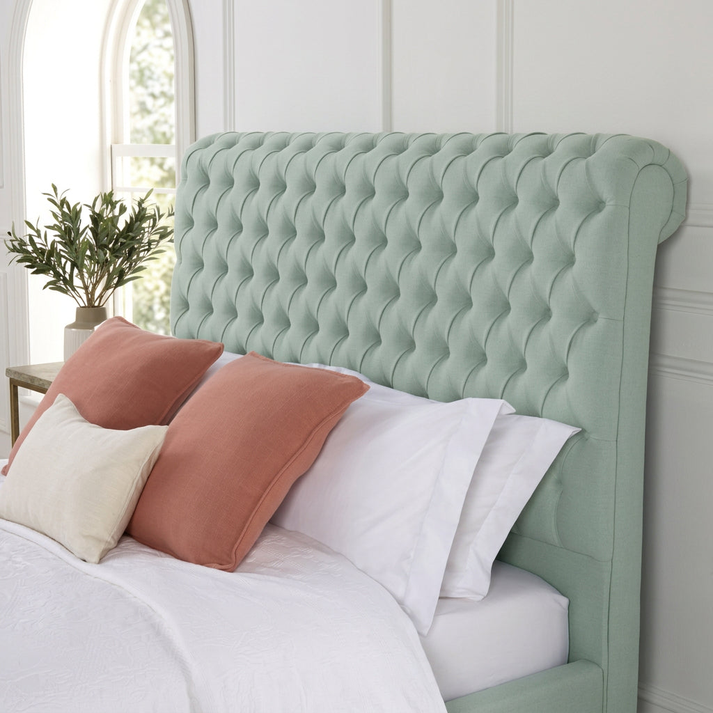 A mint green tufted velvet bed headboard styled on a bed with white bedding and accent pillows in a bright bedroom setting.
