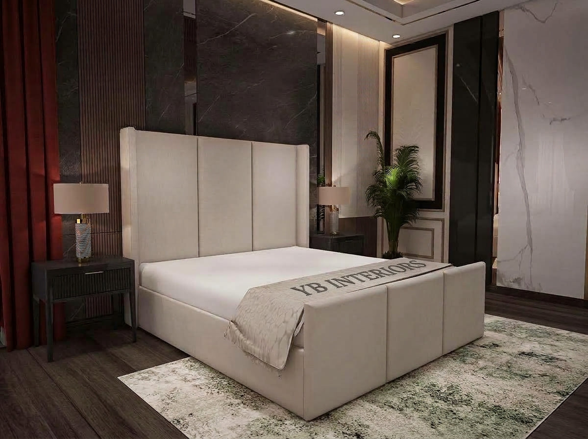 A modern upholstered bed with a tall segmented headboard and matching footboard, shown in a styled bedroom interior. The bed is dressed in white bedding with a folded cream throw that reads 'YB INTERIORS.