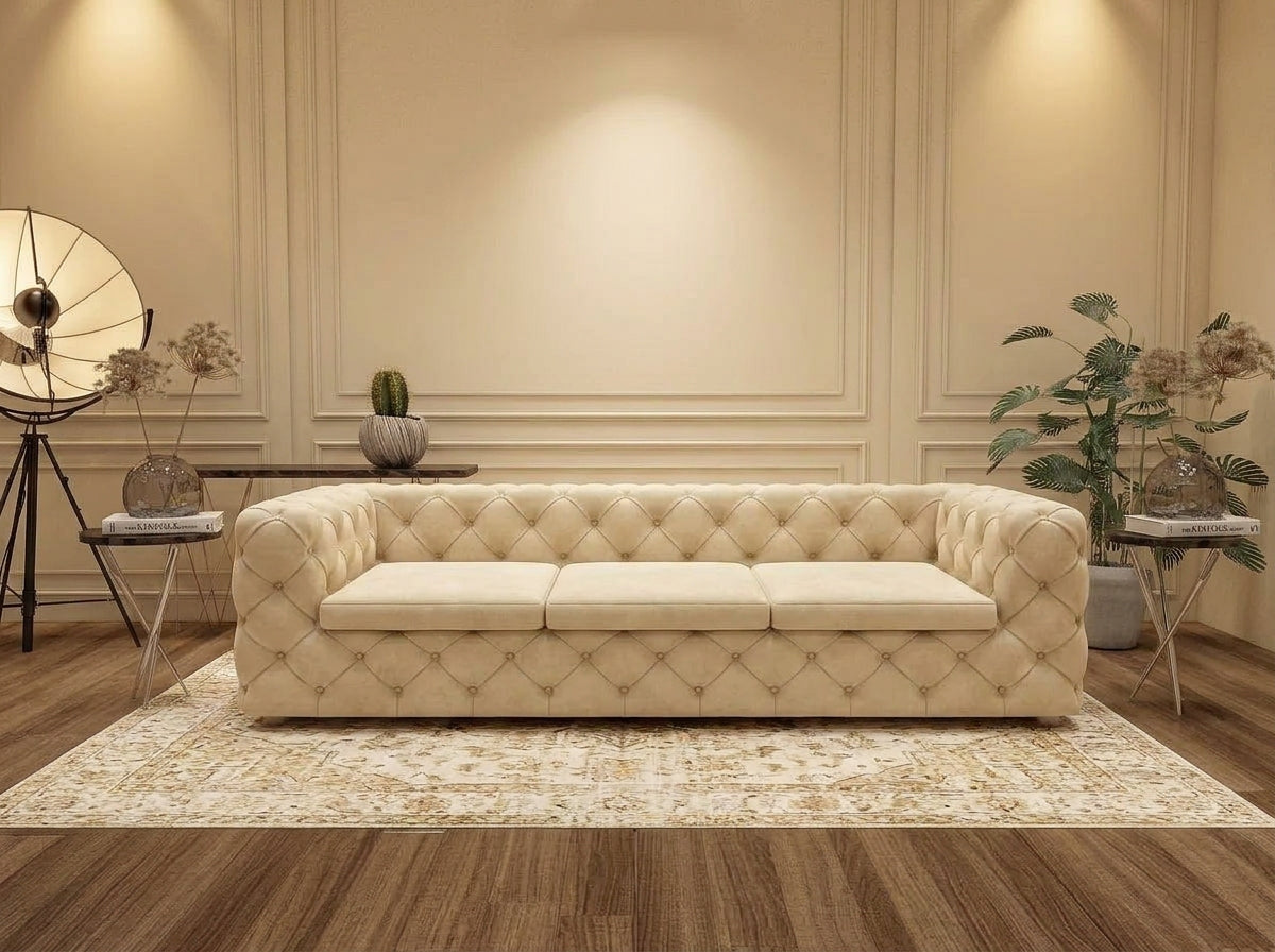A cream tufted leather sofa with three seat cushions, styled in a modern living room setting on a patterned area rug over a wood floor.