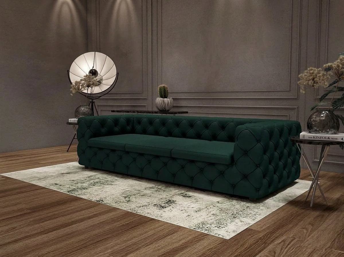 A dark green tufted velvet sofa placed on a light patterned rug in a styled living room with wood flooring, paneled walls, side tables, and decorative lamps.